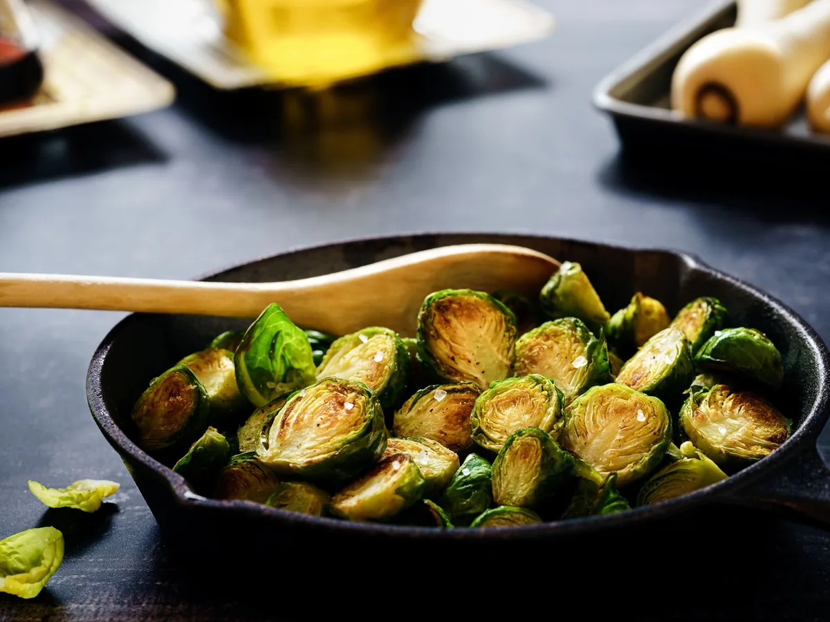 Roasted halved Brussels sprouts served in a cast iron skillet with a wooden spoon.
