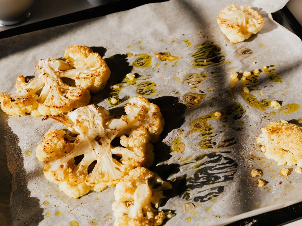 Golden roasted cauliflower slices on baking paper, seasoned with herbs and drizzled with olive oil.
