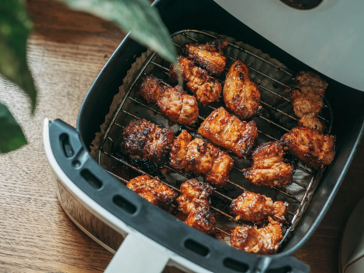 Golden-brown glazed chicken pieces cooking on the rack inside an open air fryer basket.