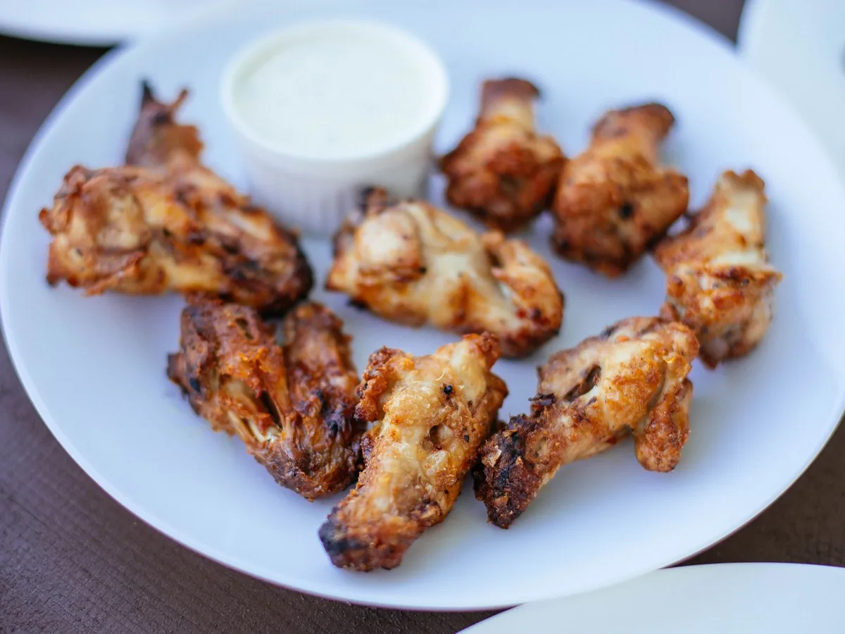 Crispy chicken wings served on a white plate with a small bowl of dipping sauce.