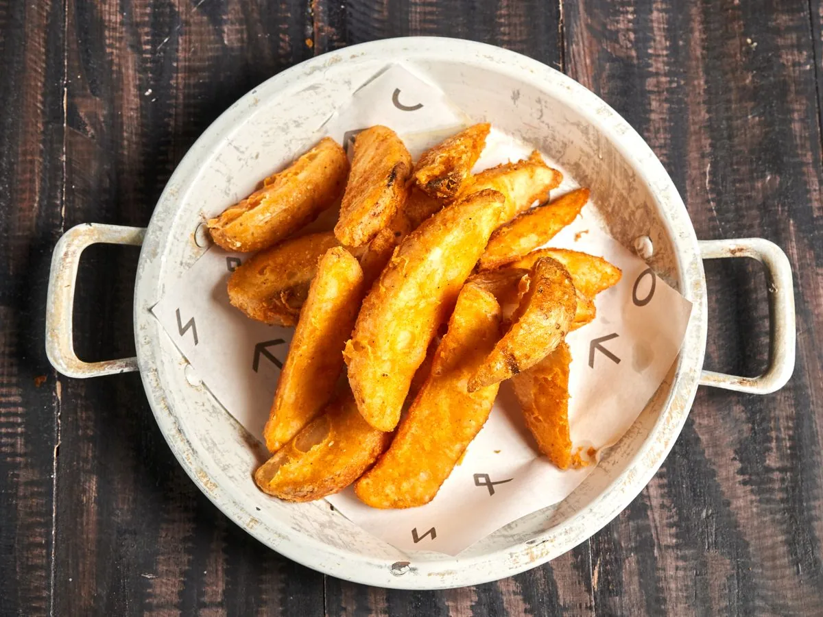 Golden crispy potato wedges served in a rustic white bowl on a wooden table.