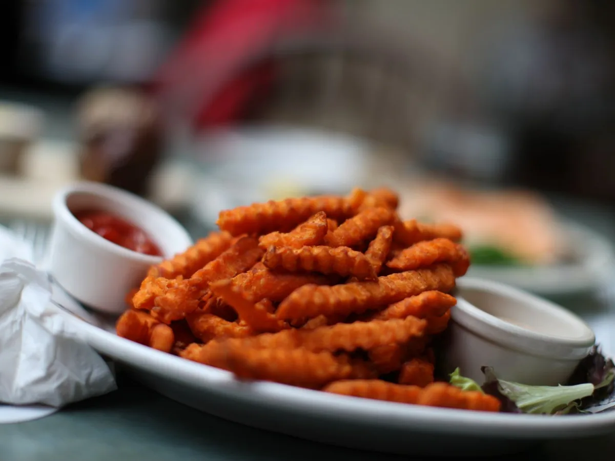 Crinkle-cut sweet potato fries piled on a white plate with ketchup and dipping sauces.