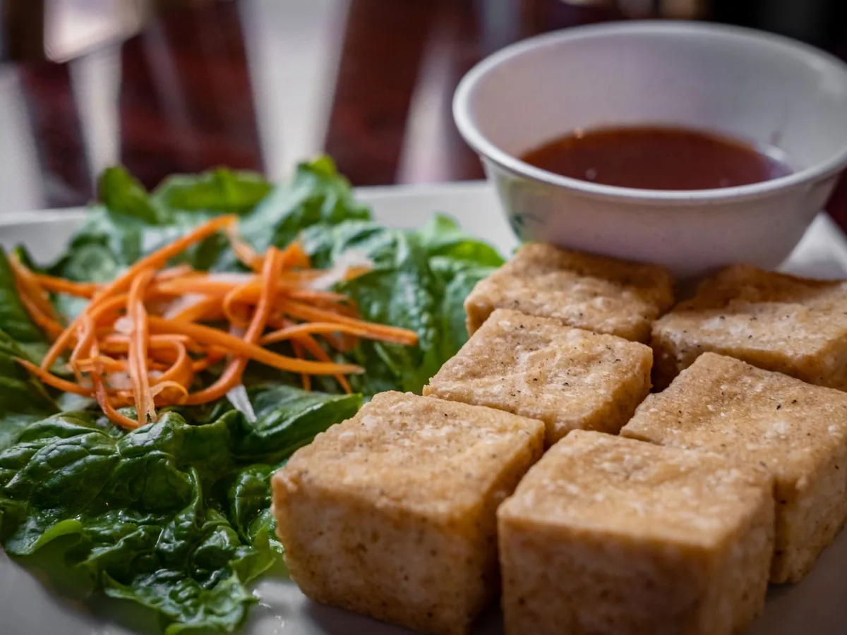 Crispy fried tofu served with fresh lettuce, carrots, and a dipping sauce on a white plate.
