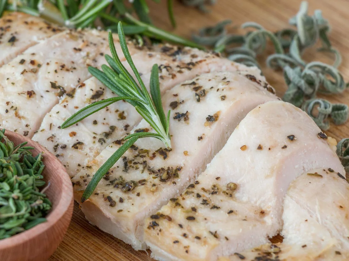 A cooked herb-crusted chicken breast with rosemary and thyme on a wooden tray