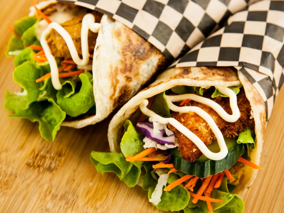 Close-up of chicken wraps filled with lettuce, cucumber, carrots and mayo on a wooden surface