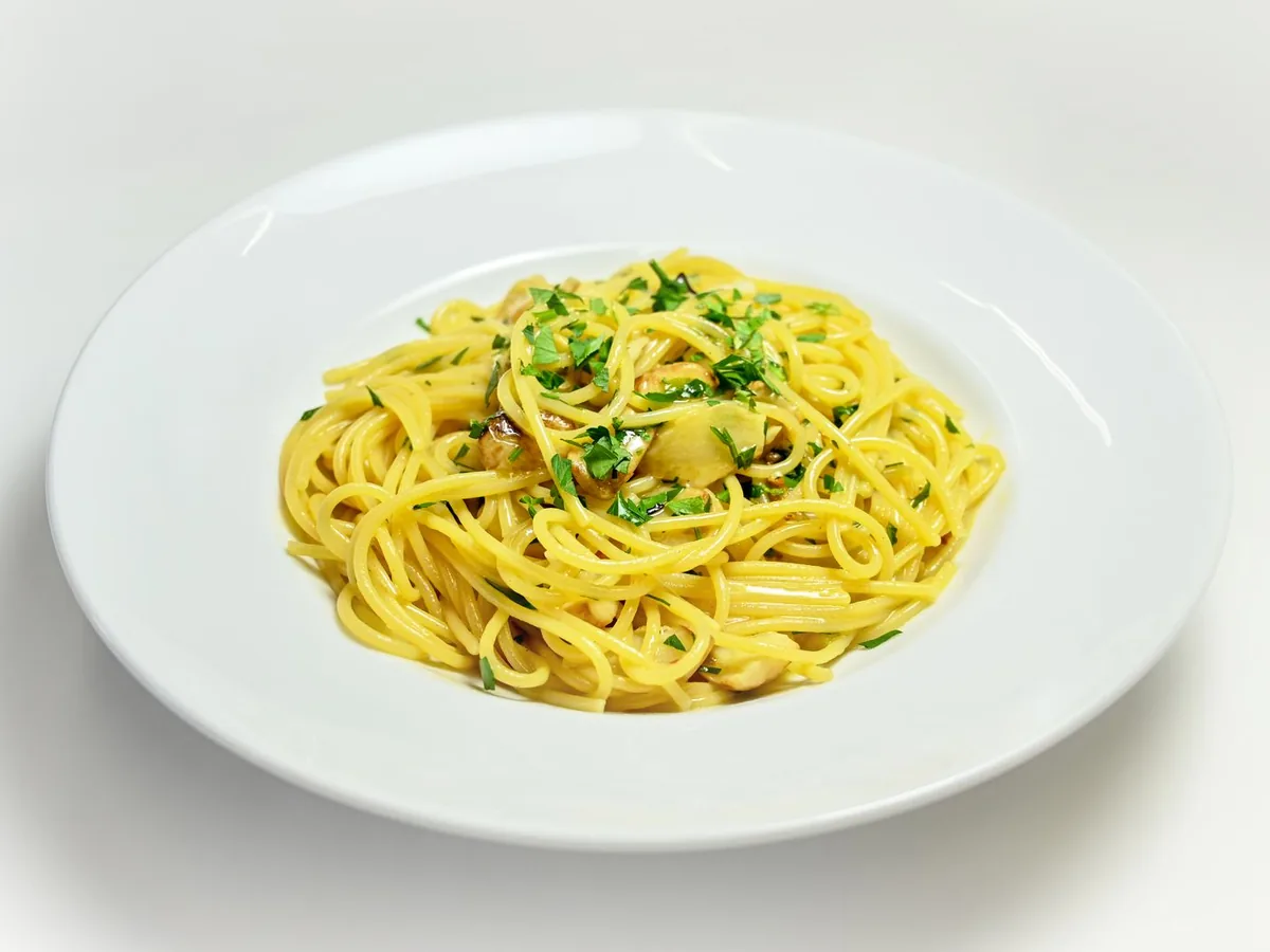 A close-up of spaghetti aglio e olio with chopped basil on a white plate