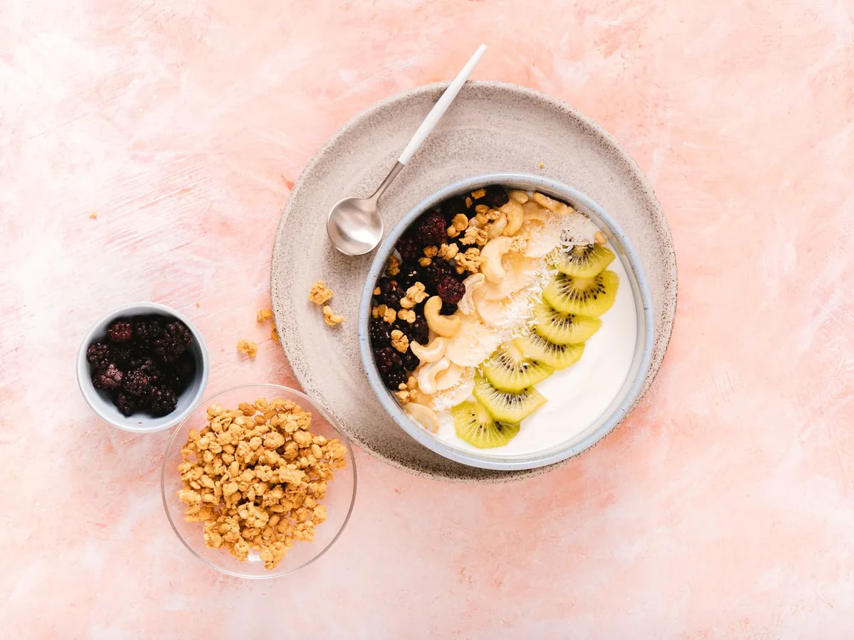 Yogurt bowl topped with sliced kiwi, berries and nuts in a ceramic bowl
