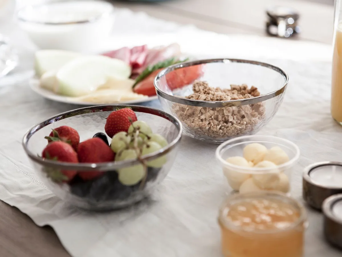 A breakfast spread with bowls of fresh fruit, granola, and glasses of juice on a dining table.
