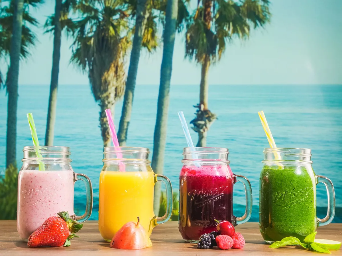 Mason jars filled with colorful fruit smoothies against a tropical ocean backdrop