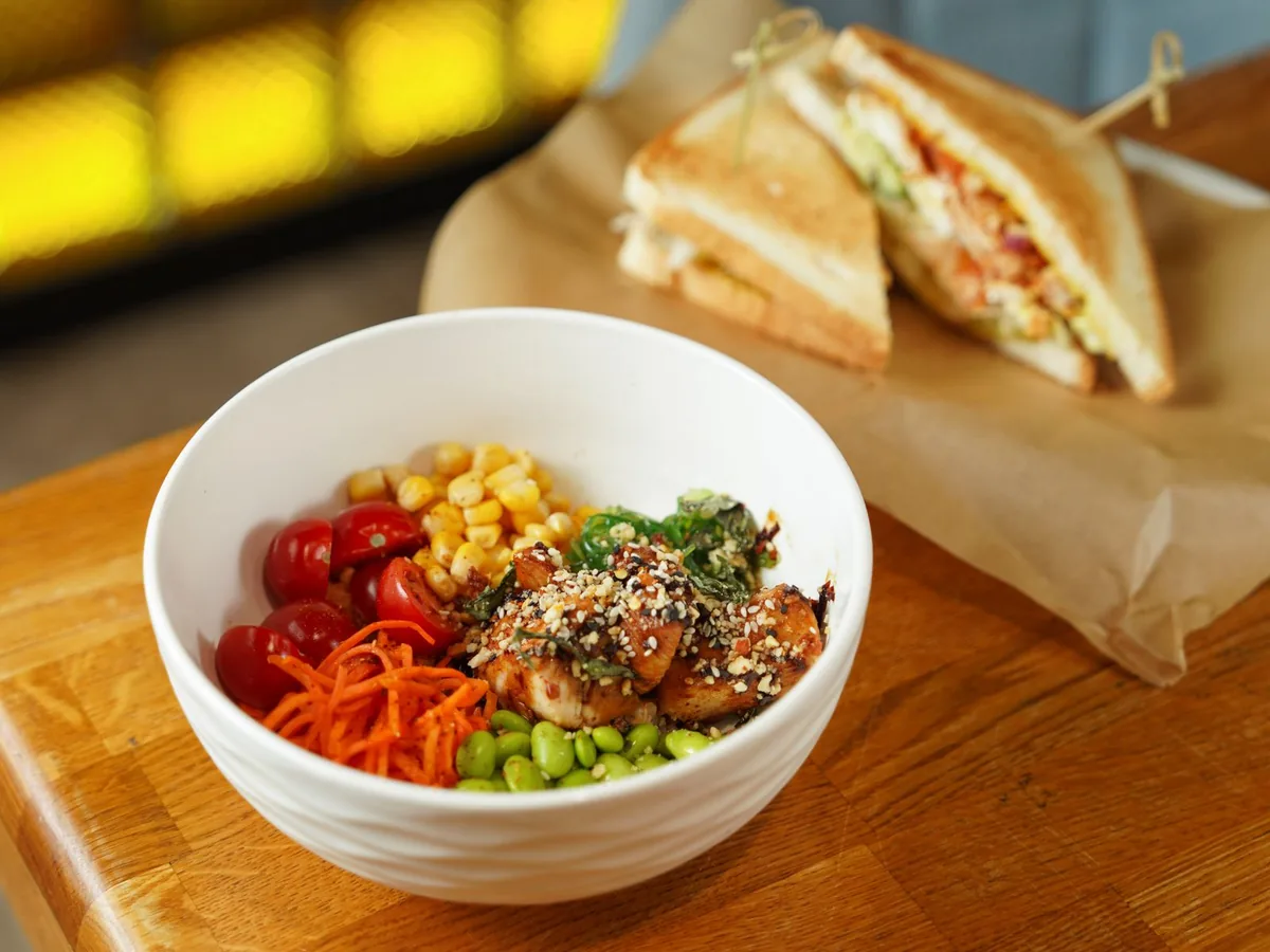A salad bowl with grilled chicken and vegetables beside toast on a wooden table.