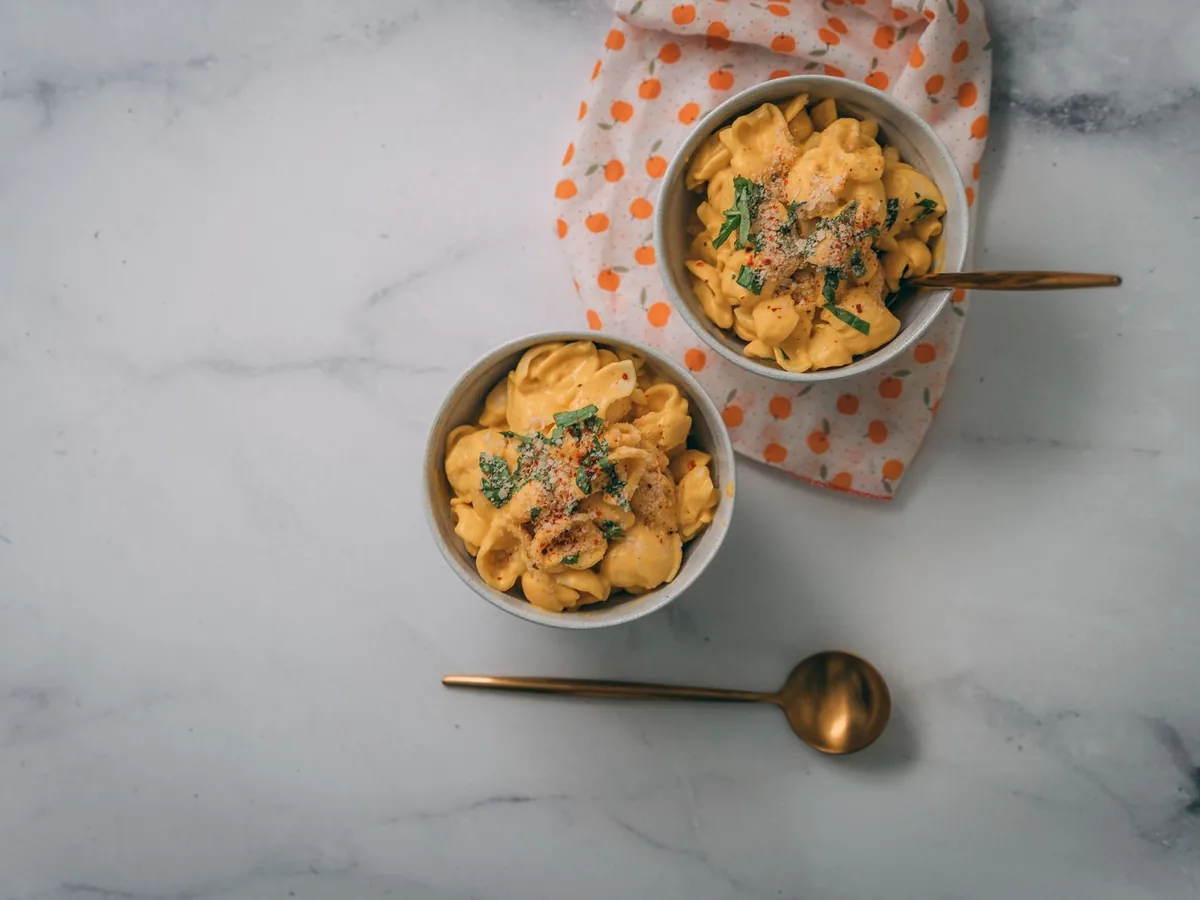 Two bowls of creamy mac and cheese garnished with herbs on a marble surface