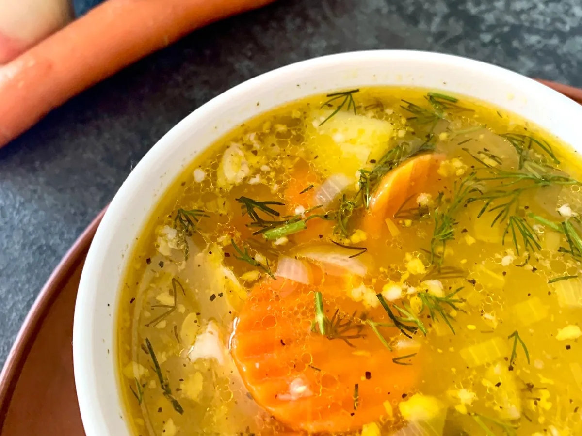A bowl of warm vegetable soup with carrots, zucchini and fresh dill
