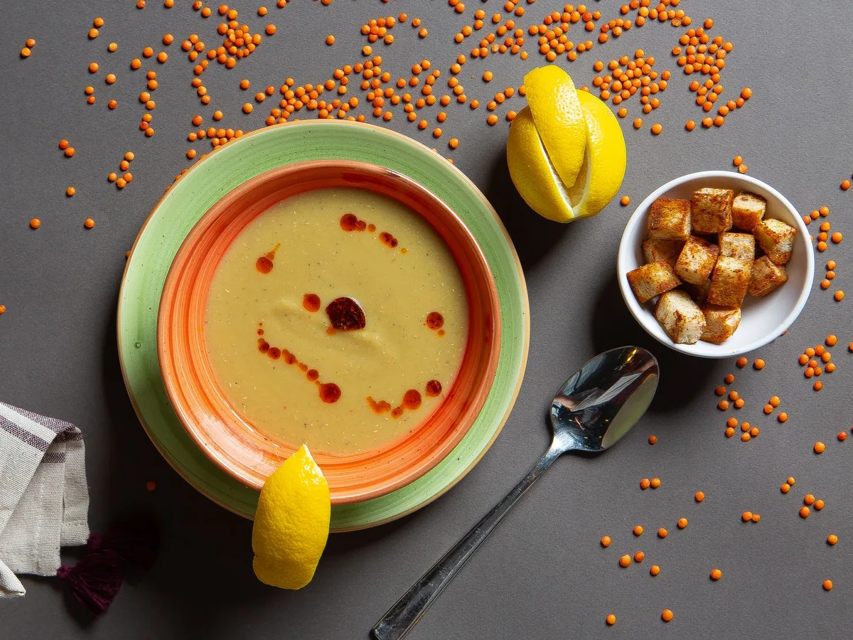 Bowl of red lentil soup with lemon wedges and croutons in a flat-lay arrangement