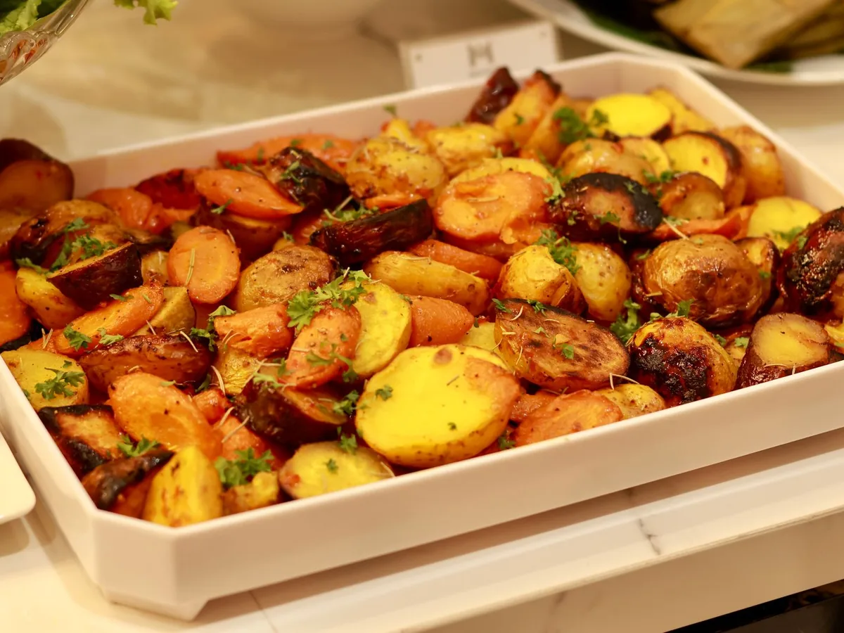A white tray of oven-roasted baby potatoes and carrot slices garnished with fresh herbs