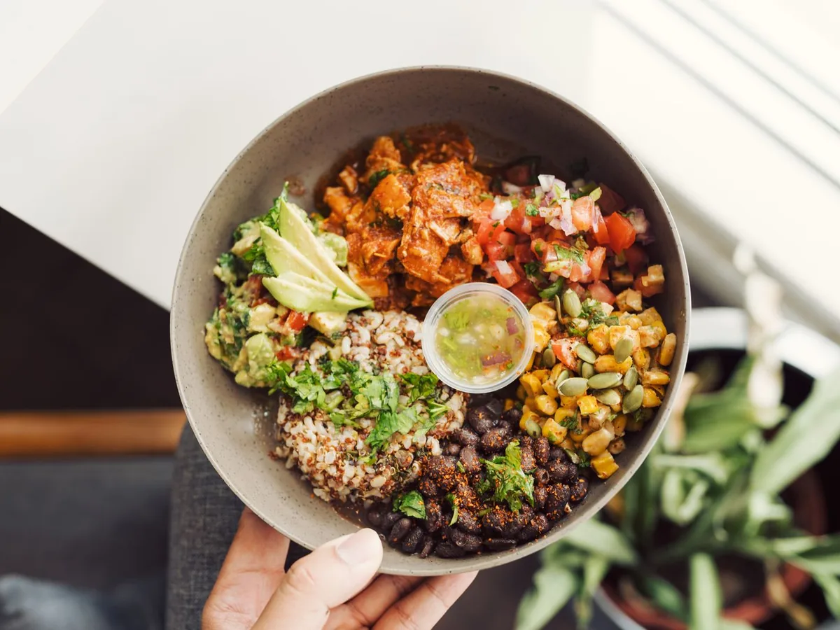 Hand holding a buddha bowl with quinoa, avocado, and fresh salsa, viewed from above