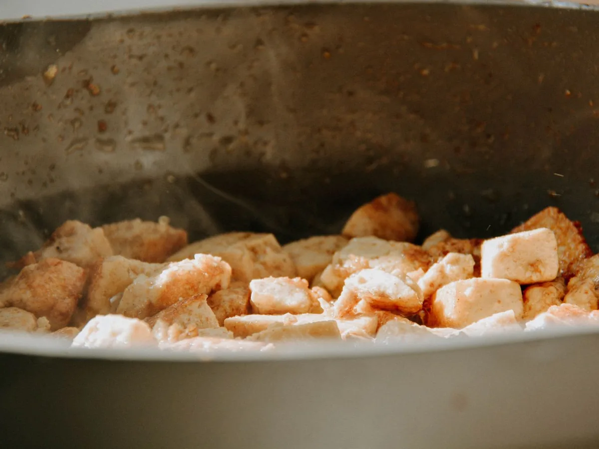 Close-up of golden tofu cubes sizzling in a frying pan
