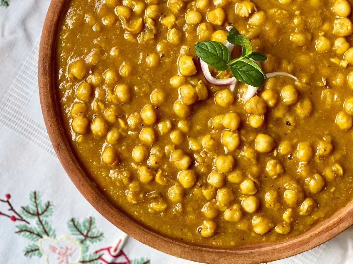 Close-up of chana masala, a chickpea curry in rich reddish-brown gravy, garnished with fresh herbs.