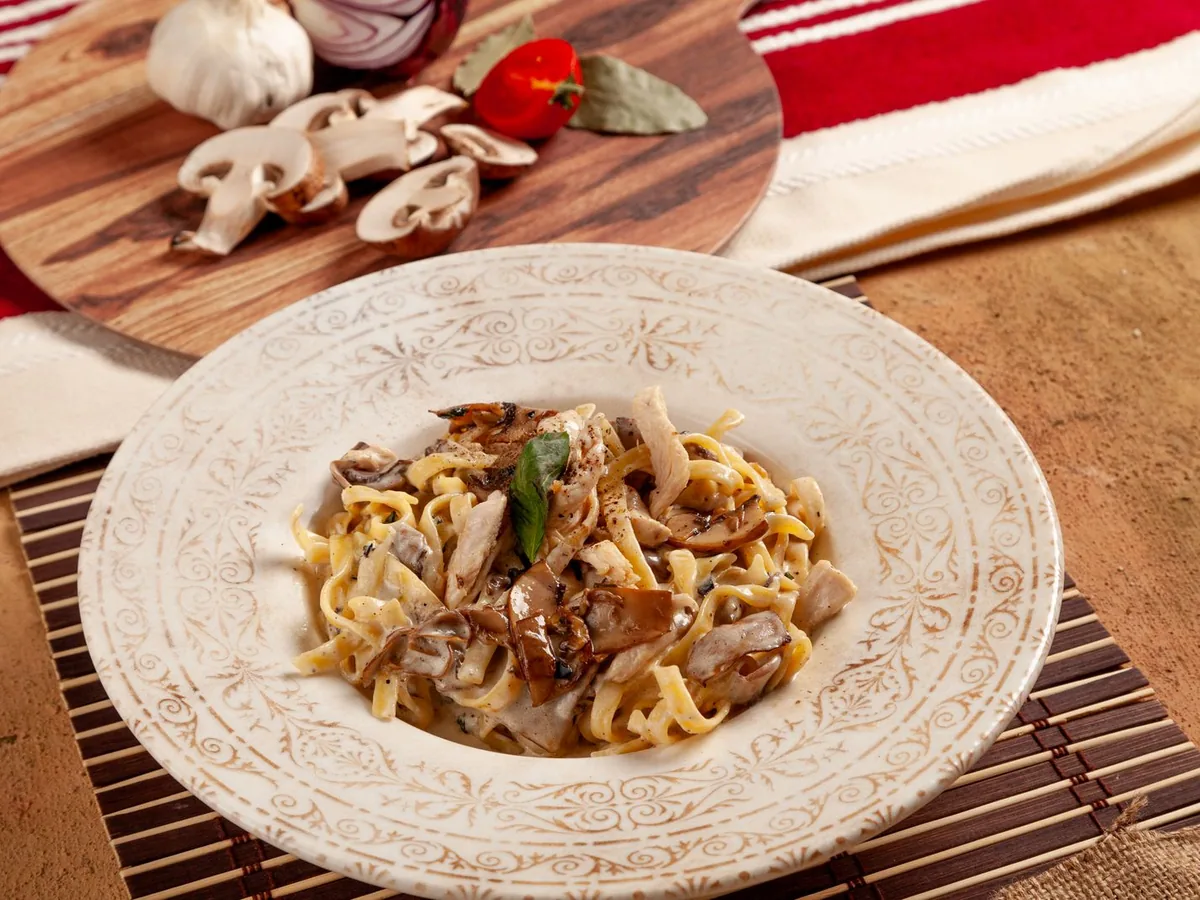 A plate of pasta coated in a creamy mushroom sauce, garnished with fresh herbs on a decorative plate.