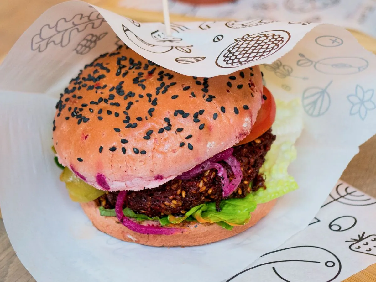 A veggie burger with a sesame seed bun, fresh lettuce, and sliced tomatoes, photographed from the side on a dark wooden surface.