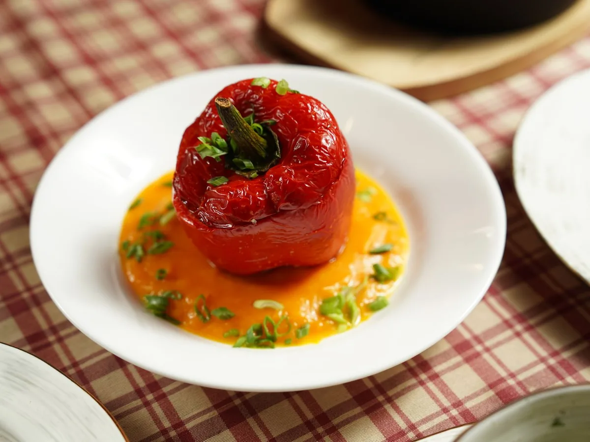 Whole roasted stuffed red bell pepper served on a creamy sauce and garnished with fresh herbs on a white plate.