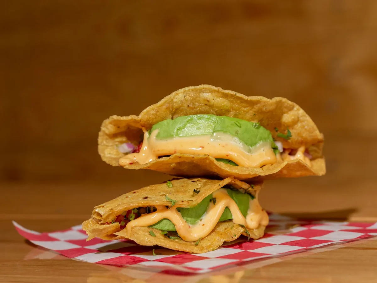Stacked vegetarian tacos filled with creamy avocado and sauce, served on checkered paper.
